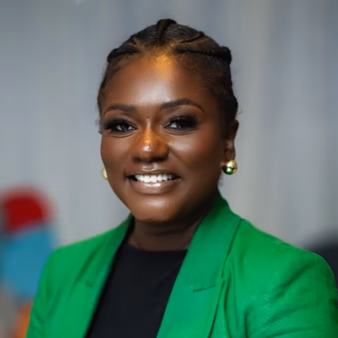 Smiling woman with braided hair wearing a green blazer and gold earrings.