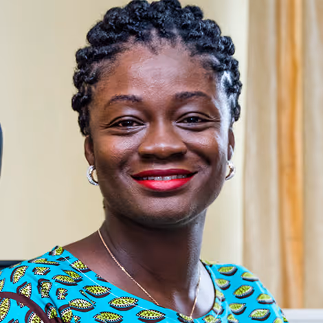 Smiling woman with braided hair wearing a vibrant patterned dress and red lipstick.