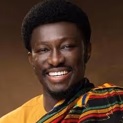 Smiling man wearing a colorful traditional patterned cloth over a yellow shirt against a brown background.