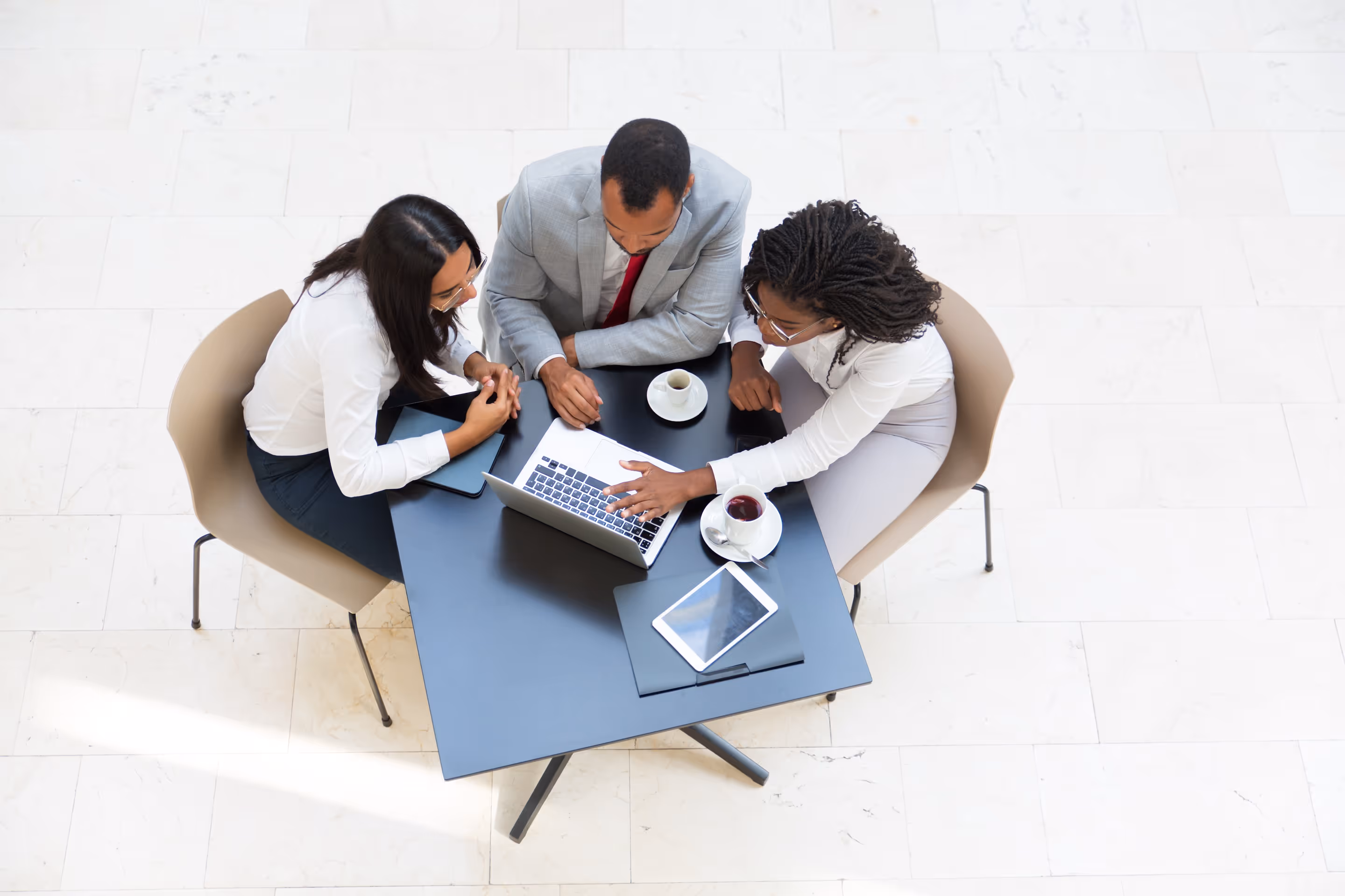 Three business colleagues seated around a table, looking at a laptop and discussing work.